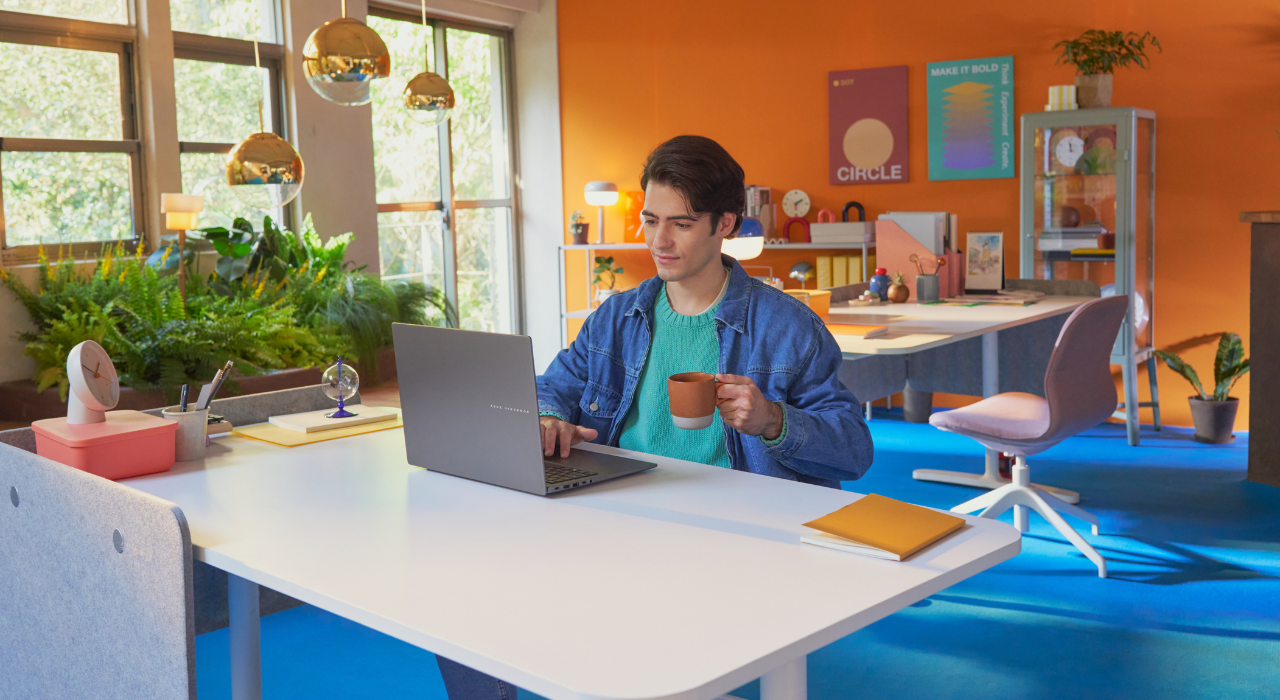 Freelancer muda bekerja santai menggunakan ASUS Vivobook S14 AI di ruang kerja modern berwarna cerah.