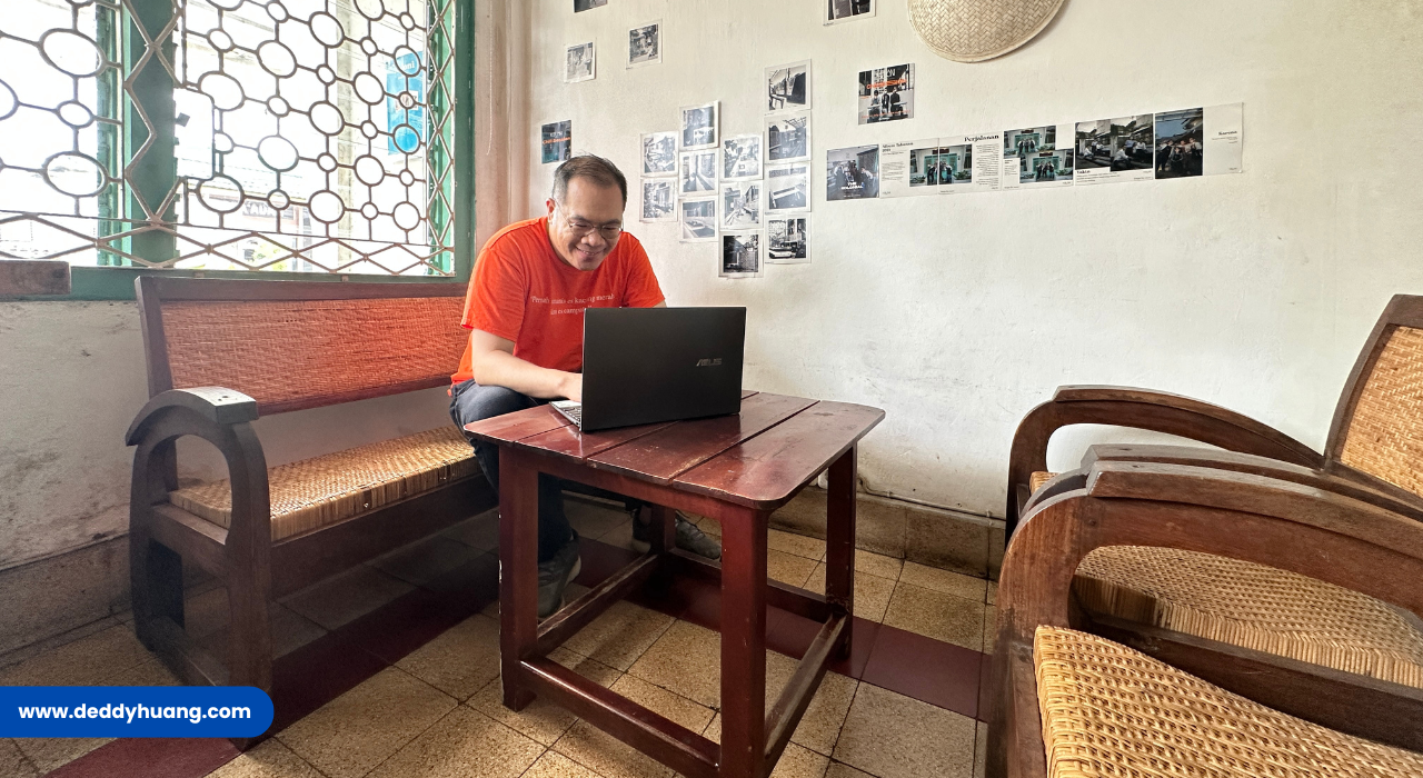 Seorang pria bekerja dengan ASUS Zenbook di ruang bergaya klasik, dikelilingi kursi rotan dan foto-foto dinding.